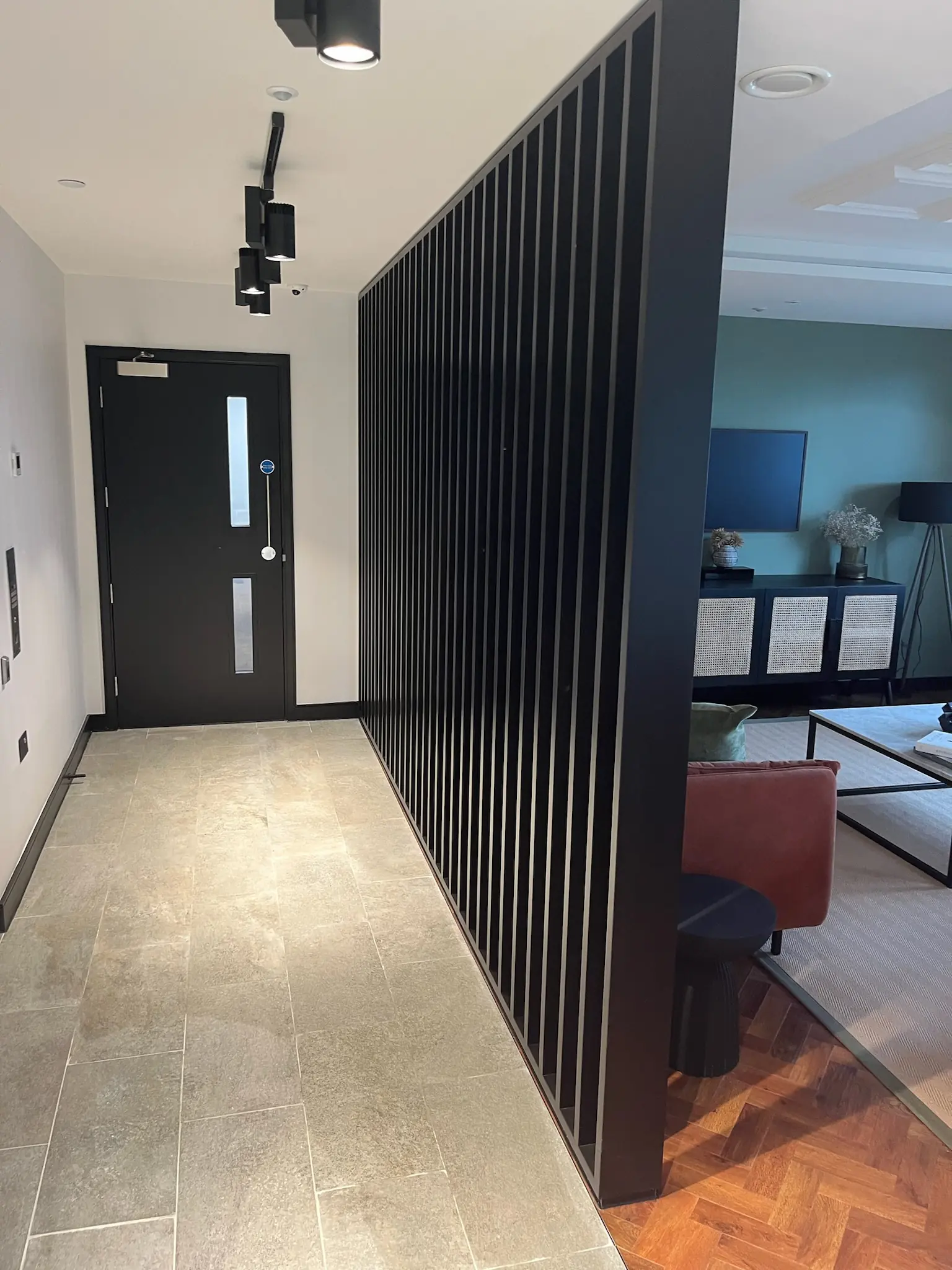 Apartment entrance hallway with black timber slat partition and stone tile flooring, London