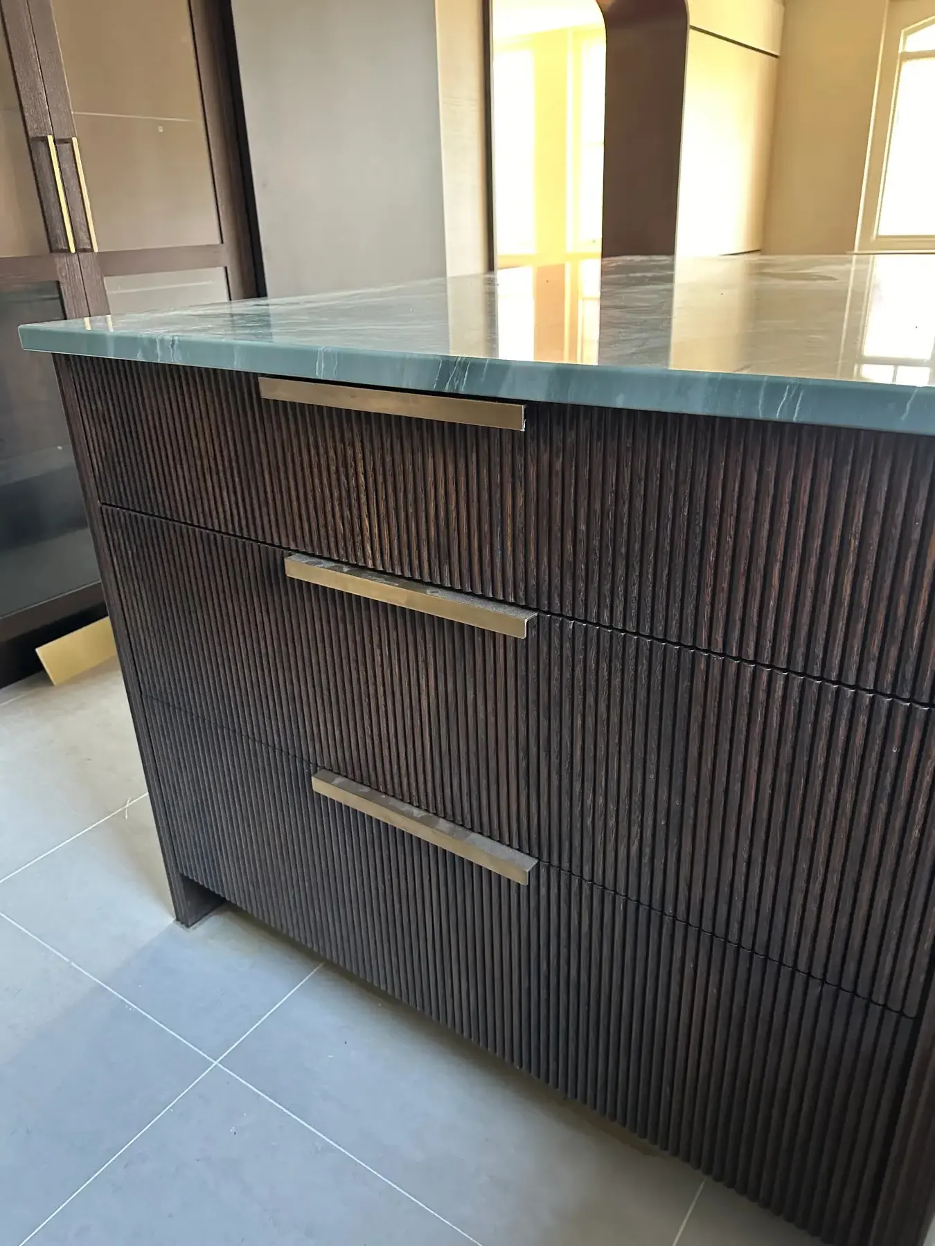 Kitchen island with fluted dark oak drawers, green onyx worktop and brass handles - London apartment refurbishment