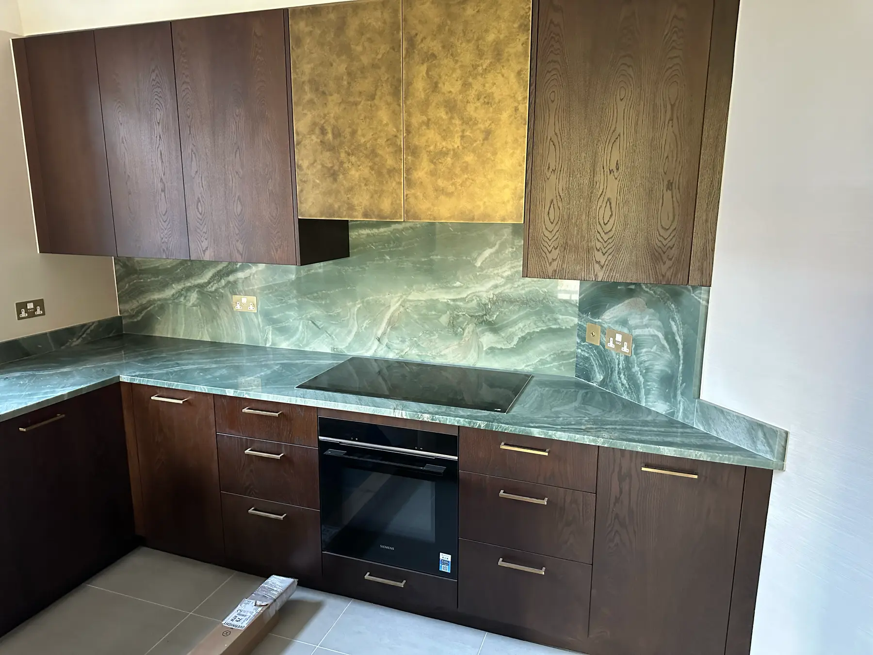 Kitchen with green onyx worktop and splashback, dark oak units and brass cabinet details - Holland Park apartment