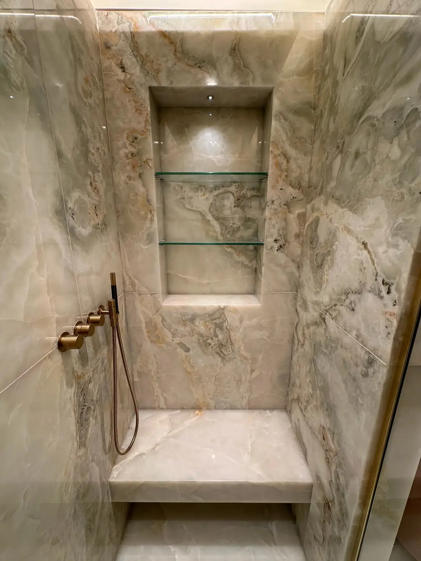 Onyx shower enclosure with lit niche, glass shelves and brass fittings - London apartment refurbishment