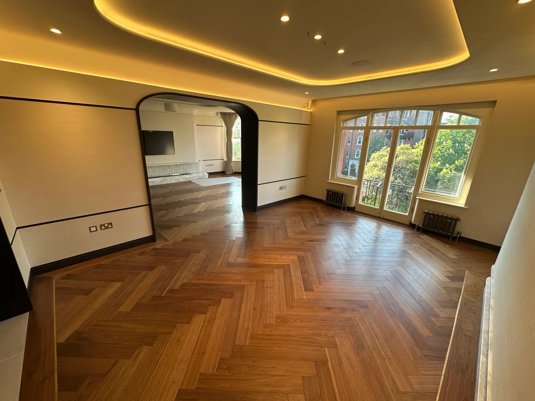 Open-plan reception room with black arch, bay windows, walnut herringbone flooring and LED ceiling - Holland Park