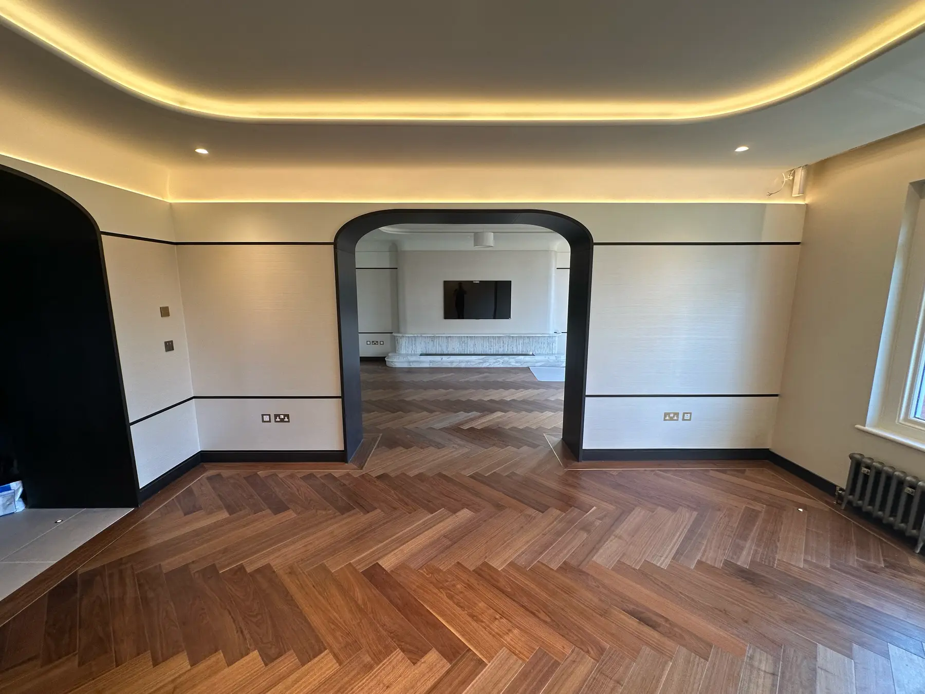 Black arch opening through to TV room with herringbone flooring and LED strip ceiling - Holland Park refurbishment