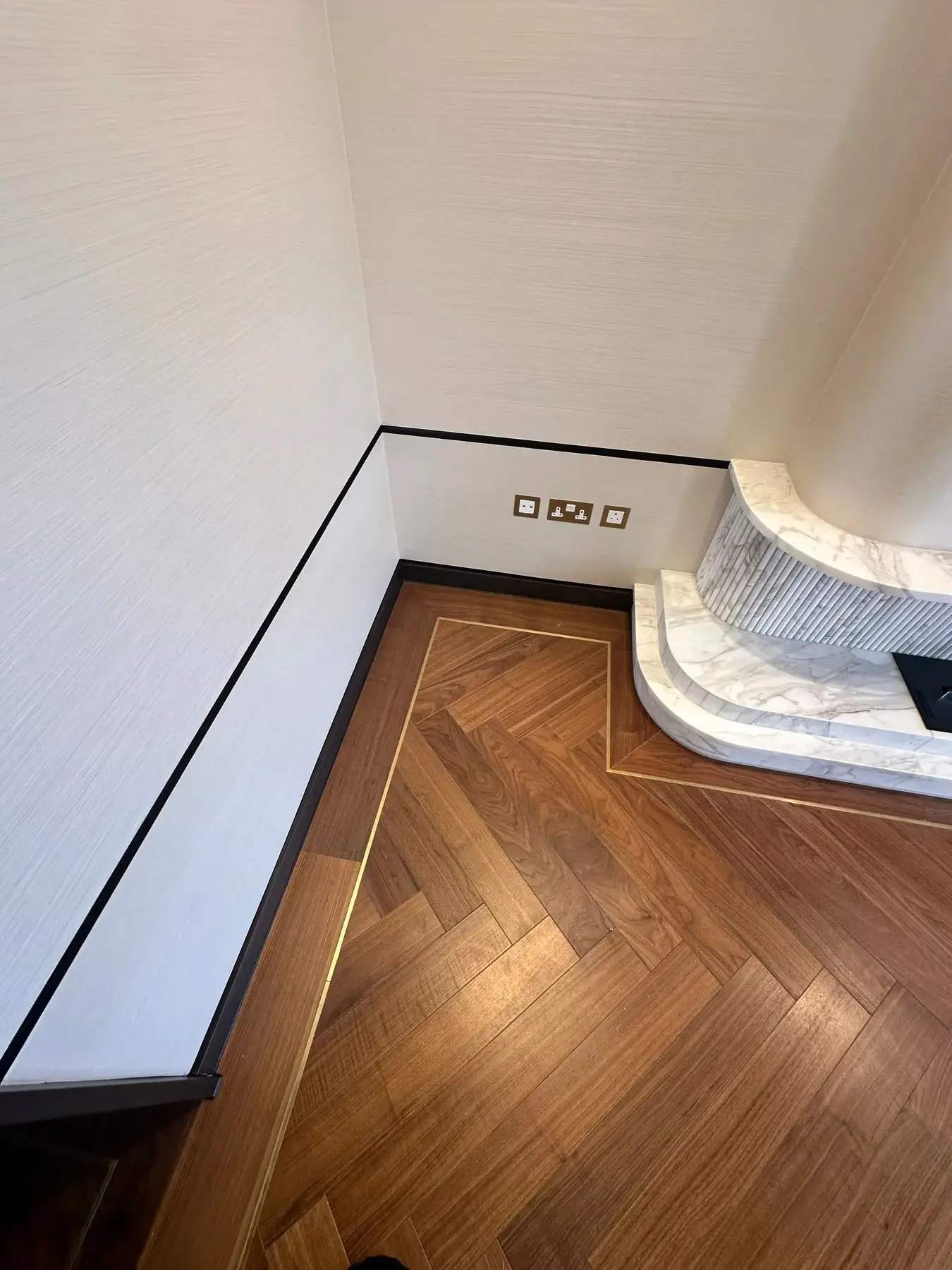 Walnut herringbone flooring with brass border inlay and marble fireplace plinth detail - London apartment